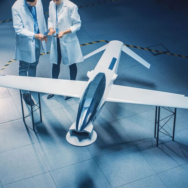 Man in white coat and person holding papers standing near flying craft