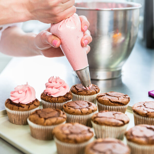 Person adding icing to cupcakes in a bakery