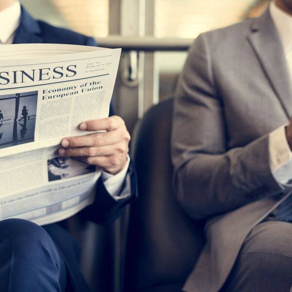 Two men in business suits and one is reading the business section of newspaper