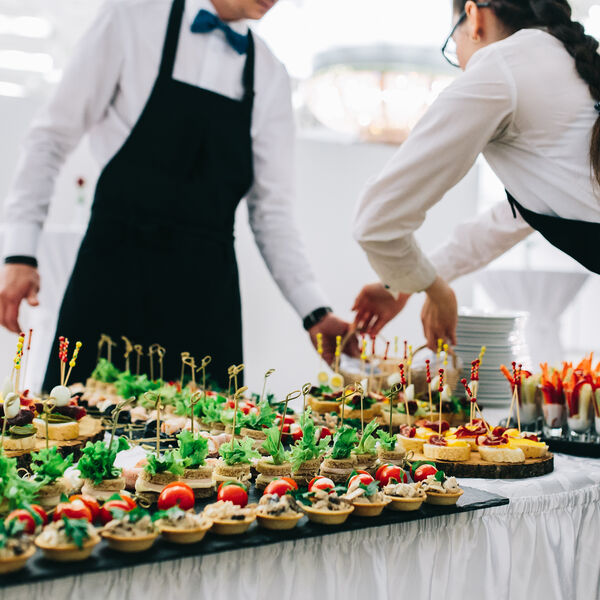 Two people in black aprons setting up a spread of food