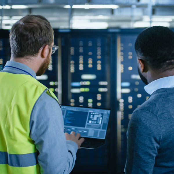 Two men looking at servers and one has a laptop in his hands