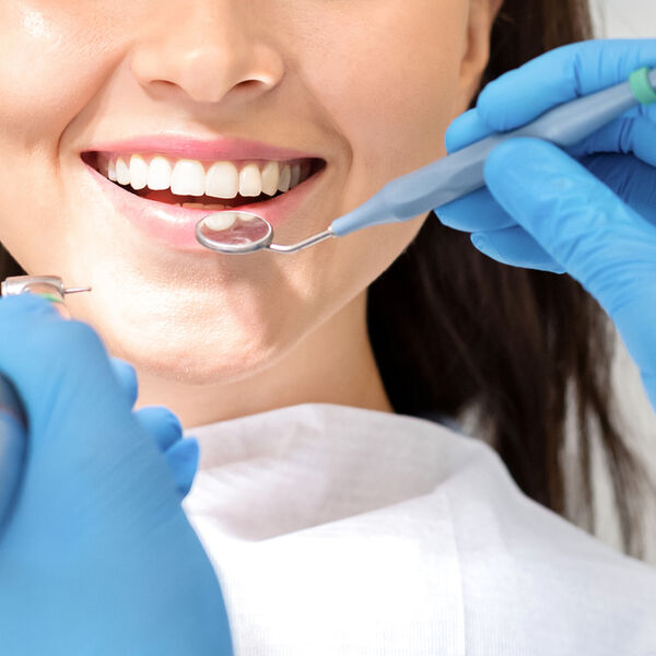 Woman with nice teeth getting her teeth examined by dentist in blue gloes