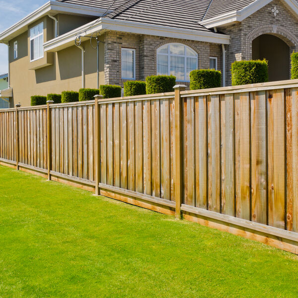 Wooden fence separating green grass and a home 