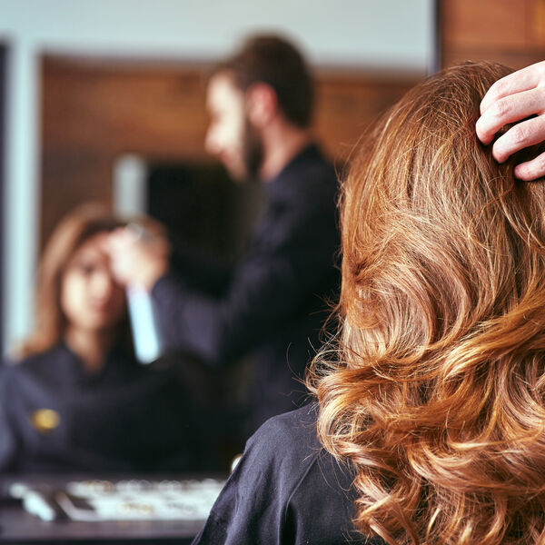 Male hair stylist styling a woman's long hair