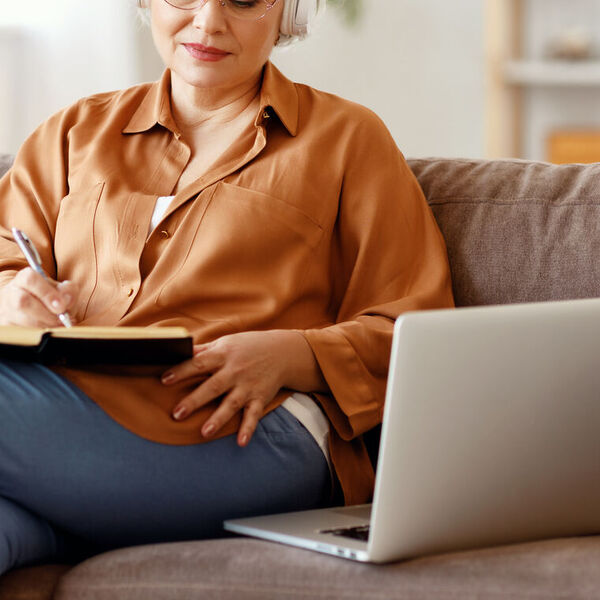 Older woman writing while doing online learning on her laptop 