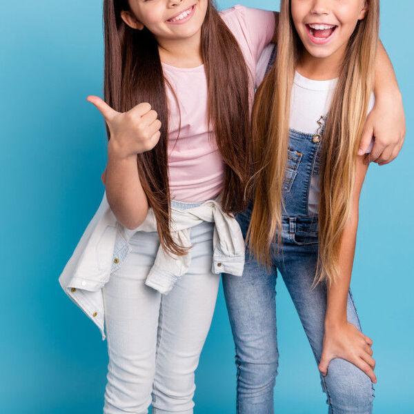 Two teen girls standing together infront of a light blue background