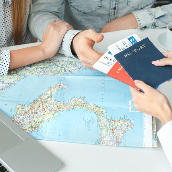 A male and woman couple sitting down with a map infront of them and a person handing their passports to them